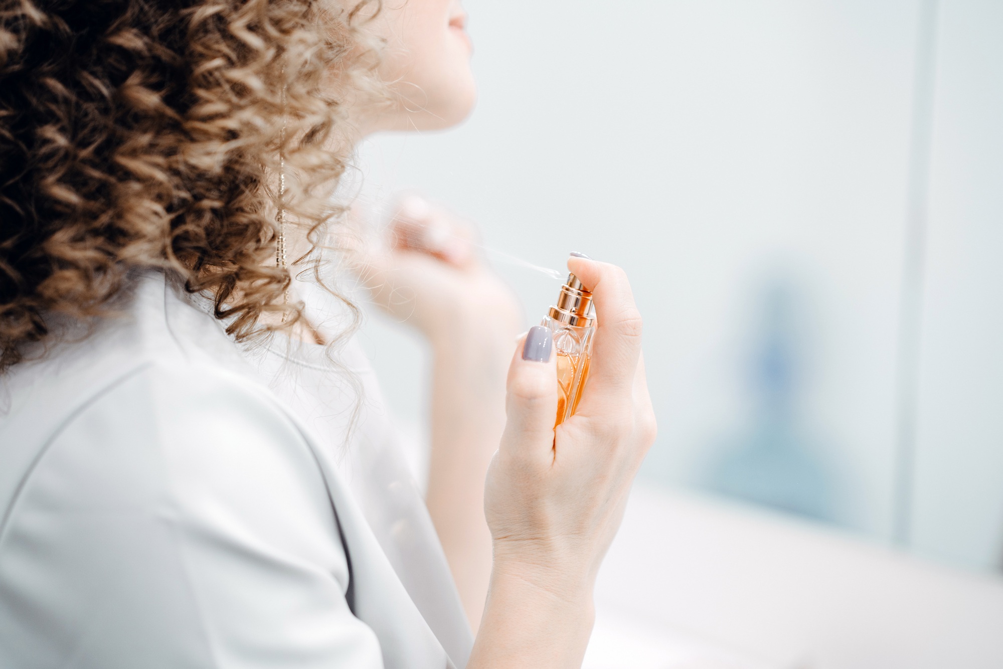 A woman with curly hair sprinkles perfume.