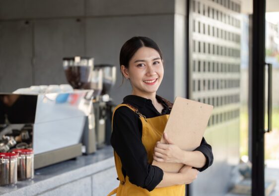 Friendly Barista Holding Clipboard in Modern Coffee Shop with Espresso Machine in Background