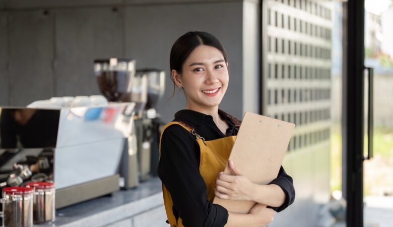 Friendly Barista Holding Clipboard in Modern Coffee Shop with Espresso Machine in Background