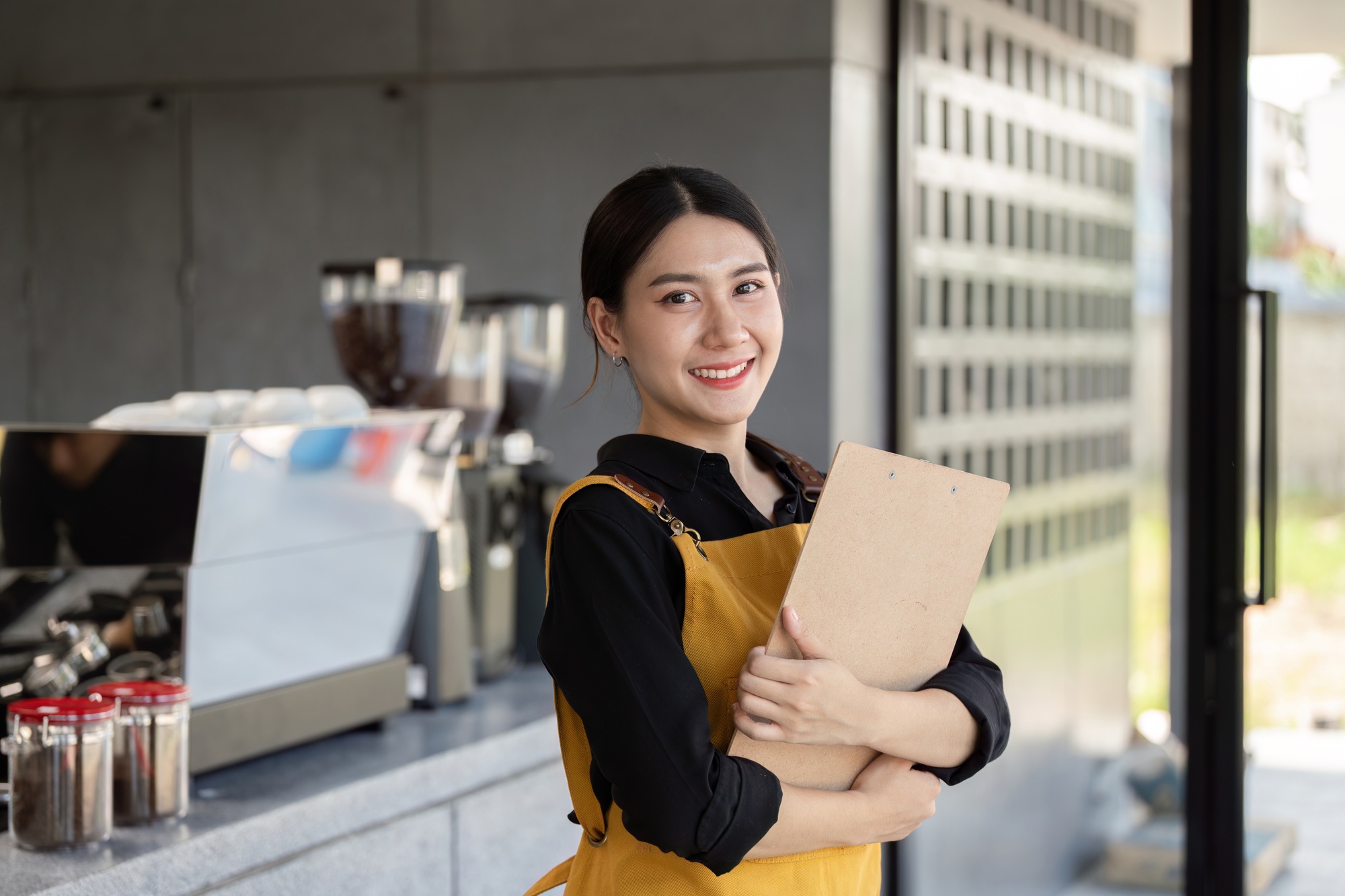 Friendly Barista Holding Clipboard in Modern Coffee Shop with Espresso Machine in Background
