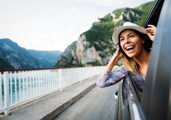 Woman in car road trip waving out the window smiling