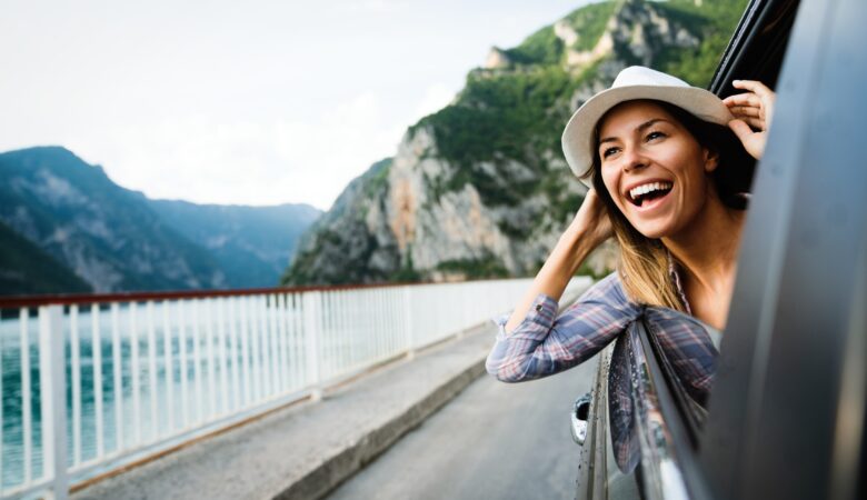 Woman in car road trip waving out the window smiling