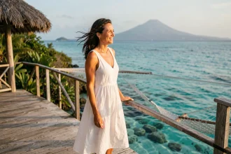 Femme élégante en robe de lin blanche sur la terrasse d'un bungalow sur l'eau dans un hôtel 5 étoiles en Guadeloupe