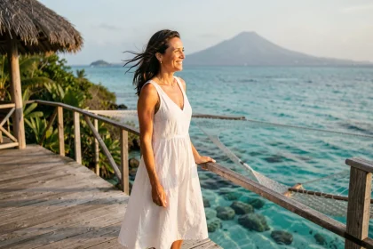 Femme élégante en robe de lin blanche sur la terrasse d'un bungalow sur l'eau dans un hôtel 5 étoiles en Guadeloupe