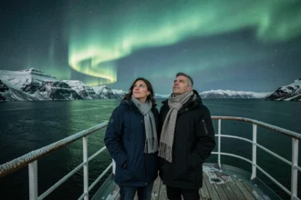 Couple sur le pont d'un navire de croisière polaire observant une aurore boréale verte au-dessus des fjords norvégiens