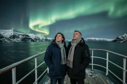 Couple sur le pont d'un navire de croisière polaire observant une aurore boréale verte au-dessus des fjords norvégiens