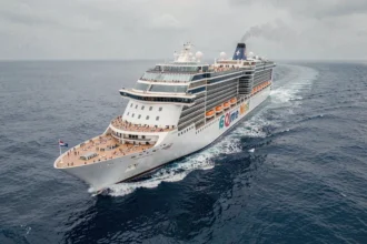 Vue aérienne d'un immense paquebot de croisière naviguant en pleine mer avec des passagers visibles sur les ponts